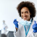 Happy African American healthcare expert wearing protective face mask and gloves at medical clinic. She is looking at the camera.