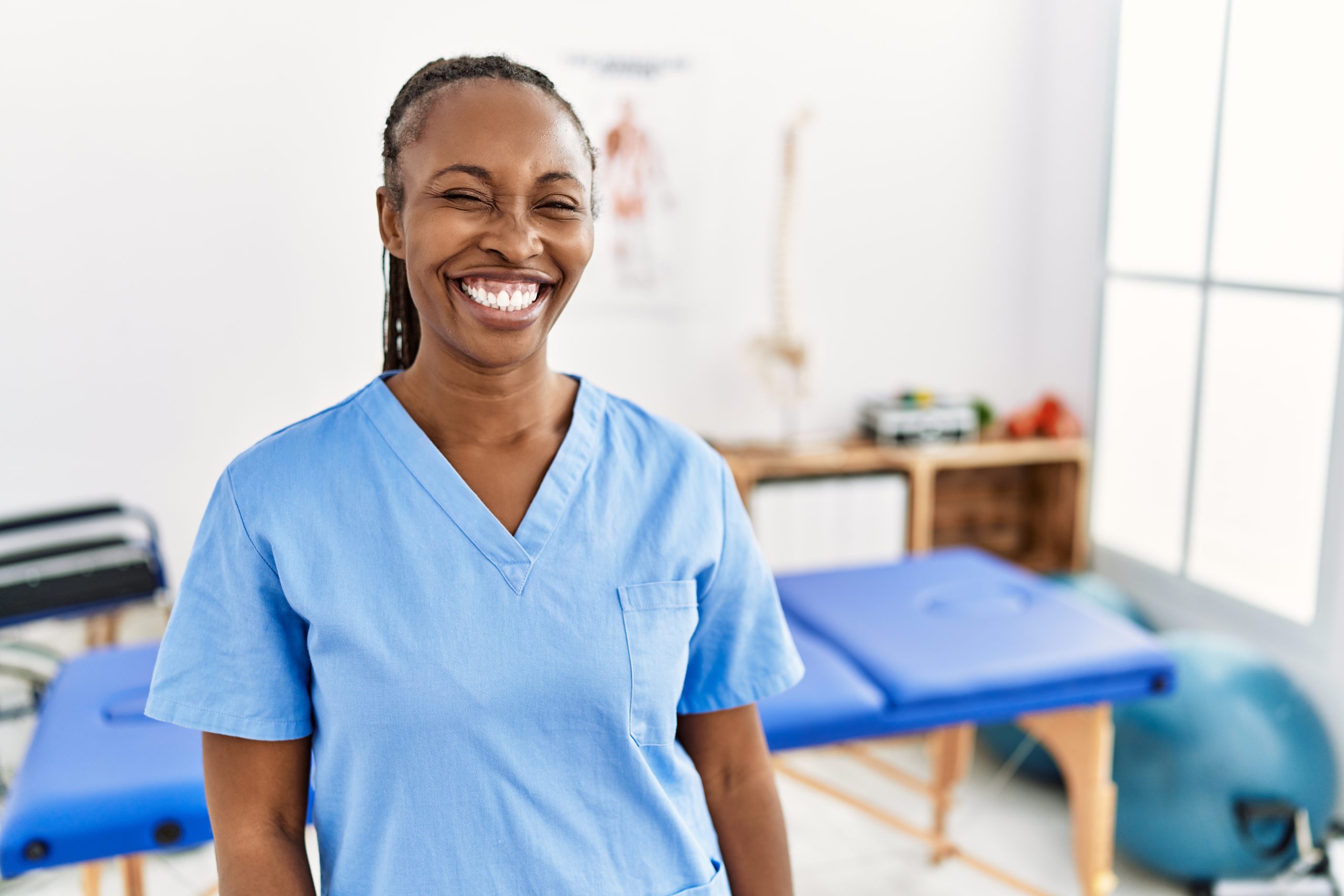 Black woman with braids working at pain recovery clinic winking looking at the camera with sexy expression, cheerful and happy face.